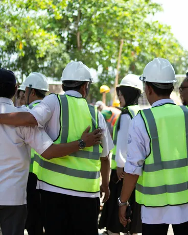 A construction crew in hard hats and high-visibility vests standing together on site, seen from behind