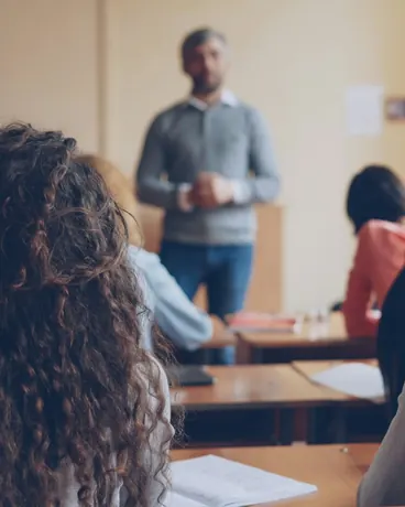 A teacher leading a class, seen from the back of the room behind the students