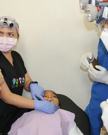 A dental team in scrubs, masks and gloves working together over a patient in the chair